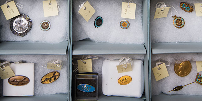 An archival storage box holds the Archives’ jewelry and pin collection, including class rings, charms, and other symbolic items. 