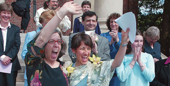 Ellen Wade ’70 (right) and Maureen Brodoff wave to cheering well-wishes on the steps of Newton, Mass., City Hall following their May 17, 2004, marriage ceremony. Duaghter Katie Wade-Brodoff stands clapping at far right. 