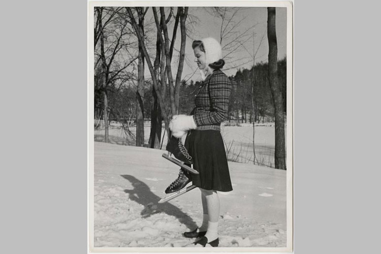 Student standing near the bank of frozen Lower Lake, holding ice skates, 1941.
