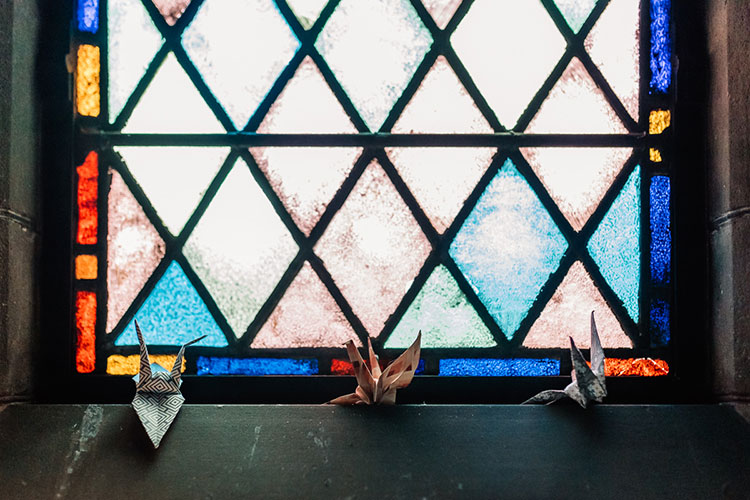 Three paper cranes positioned next to a stained glass window