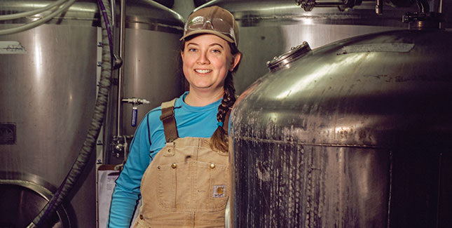 Photo fo Kate Telman in overalls with brewing stills