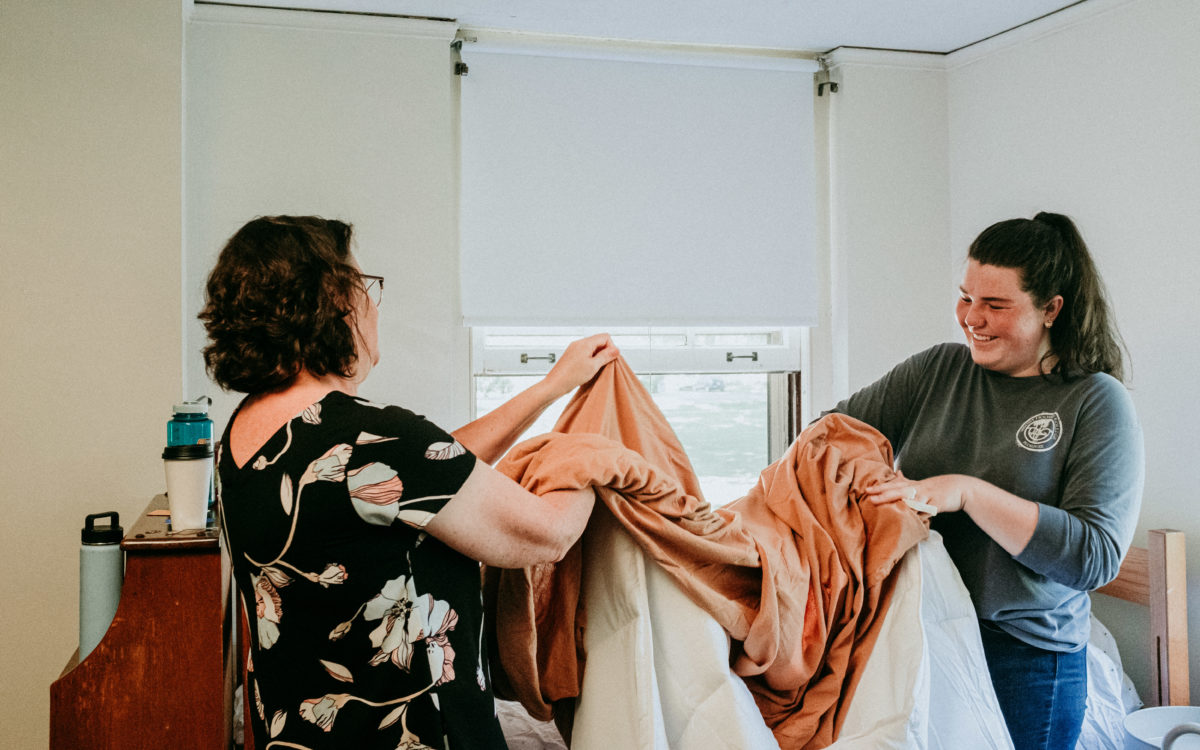 A student and their parent unfolds a set of orange and white bedsheets.