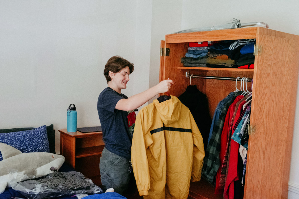 A student hangs up a yellow windbreaker in their armoire.