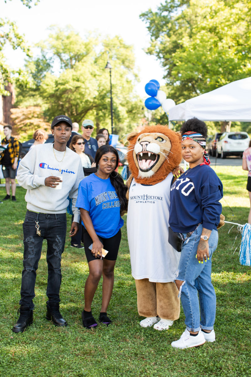 A student and family poses with Paws, the lion mascot, by the Orientation welcome tent.