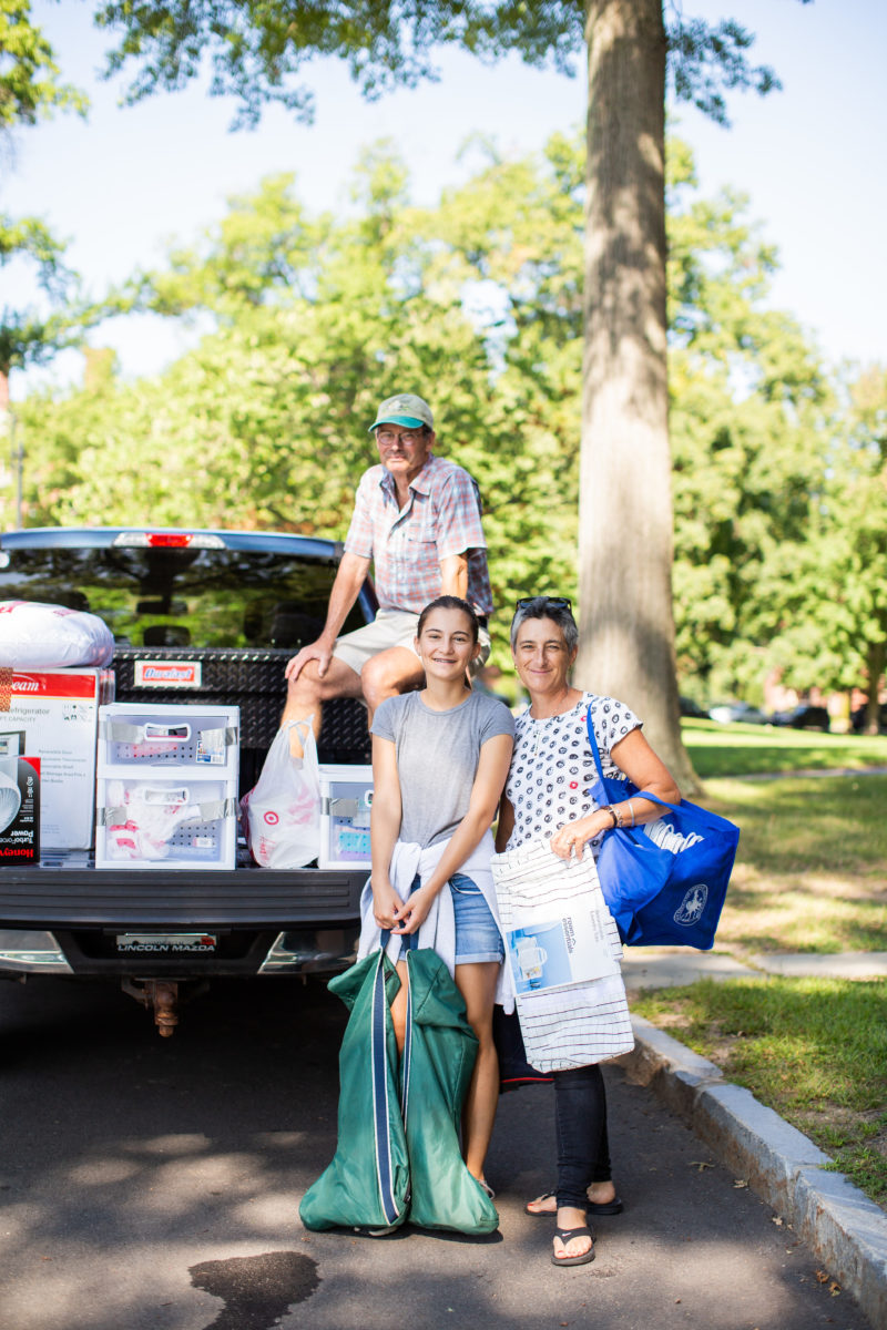 A student smiles with their parents in front of a truck bed loaded with dorm supplies.